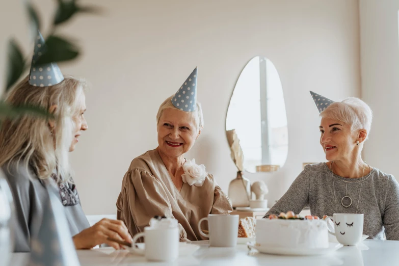 a group of older women sitting around a table, by Emma Andijewska, pexels contest winner, wearing a party hat, avatar image, background image, grey