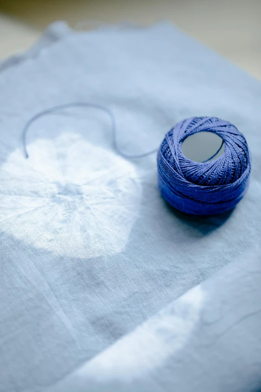 a spool of thread sitting on top of a piece of paper, a cross stitch, inspired by Louise Bourgeois, unsplash, process art, blue clothing, with backlight, porcelain organic tissue, round-cropped