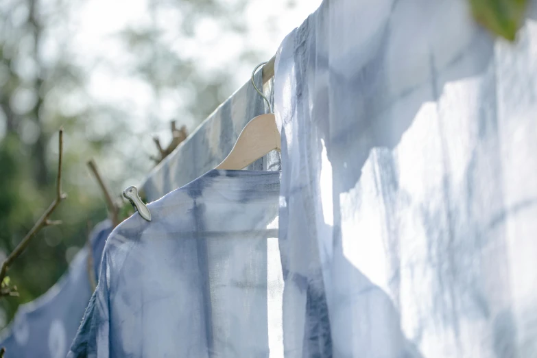 clothes hanging on a clothes line with trees in the background, a silk screen, inspired by Camille Souter, unsplash, process art, soft grey and blue natural light, ethereal curtain, detail shot, indigo