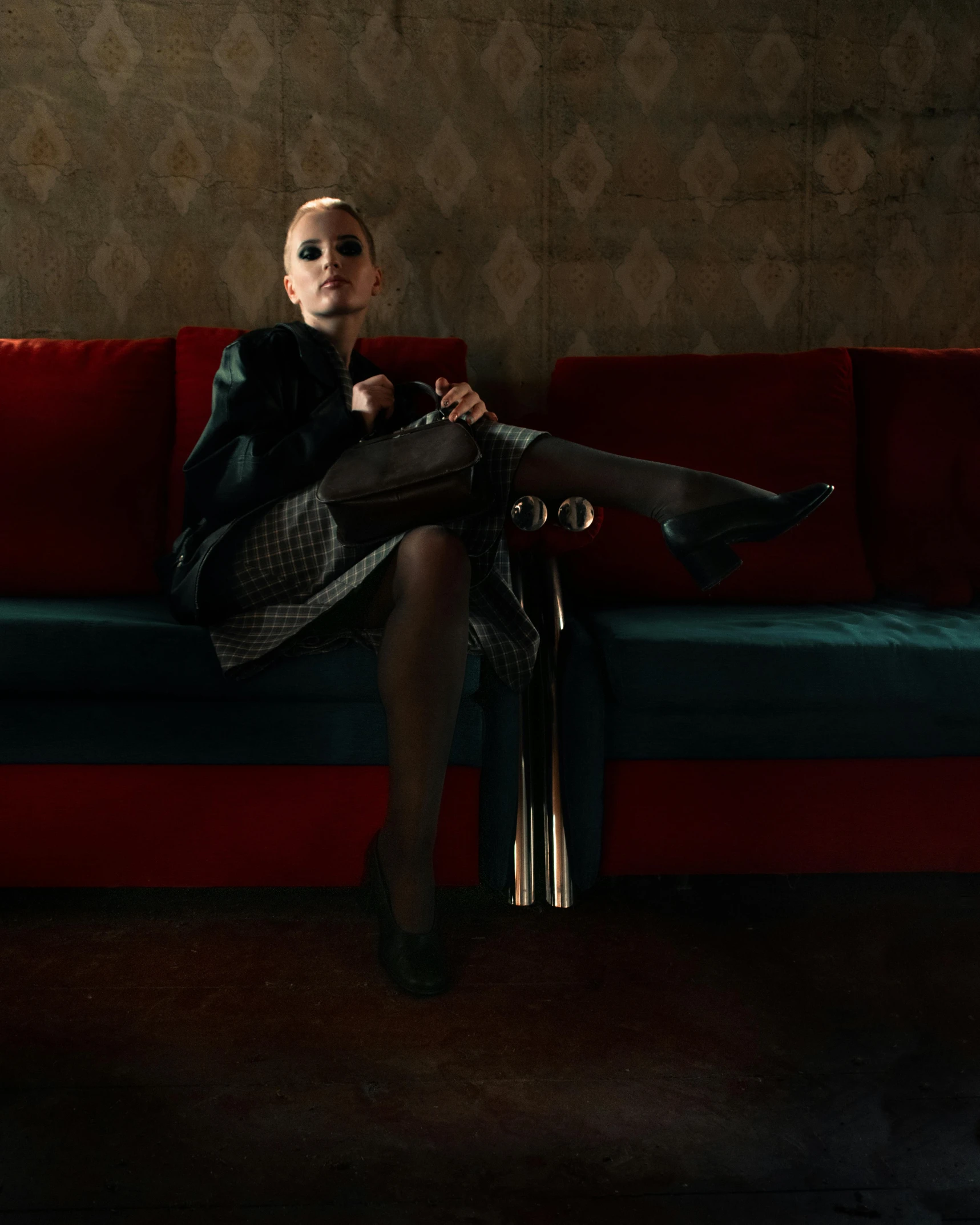 a woman sitting on a red and green couch, inspired by Helmut Newton, unsplash, lady in black coat and pantyhose, evan rachel wood, in a dark dusty parlor, leather and suede