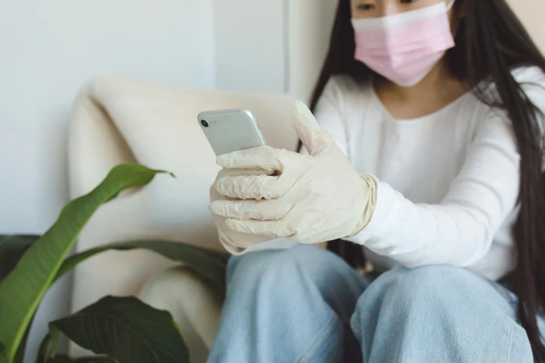 a woman sitting on a couch holding a cell phone, trending on pexels, medical mask, white gloves, avatar image, asian human