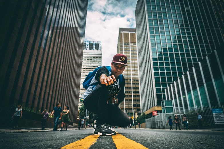 a man riding a skateboard down a street next to tall buildings, a picture, pexels contest winner, avatar image, looking at camera, crouching, taking a picture