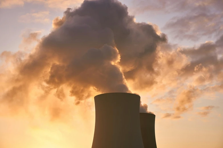 a couple of cooling towers with smoke coming out of them, by Alison Geissler, unsplash, nuclear art, taken at golden hour, shodan, profile image, getty images