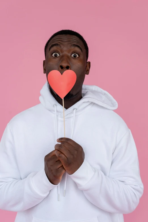 a man holding a paper heart in front of his face, an album cover, trending on pexels, romanticism, lollipops, mkbhd, plain background, pink iconic character