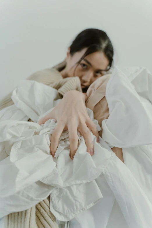 a woman laying on top of a bed covered in white sheets, unsplash contest winner, visual art, hands shielding face, layered skirts, made of lab tissue, model wears a puffer jacket