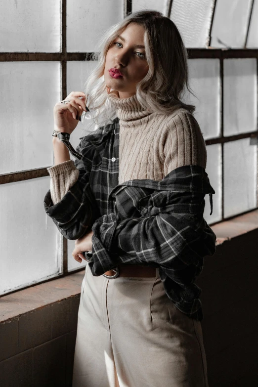 a woman standing in front of a window, trending on pexels, baroque, wearing plaid shirt, grey sweater, realistic »