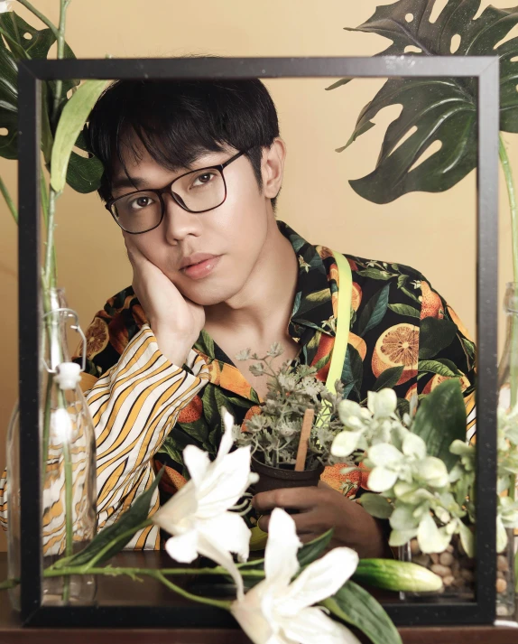 a man sitting in front of a mirror with flowers, an album cover, inspired by David Diao, wearing black frame glasses, next to a plant, in style of lam manh, he is about 20 years old | short