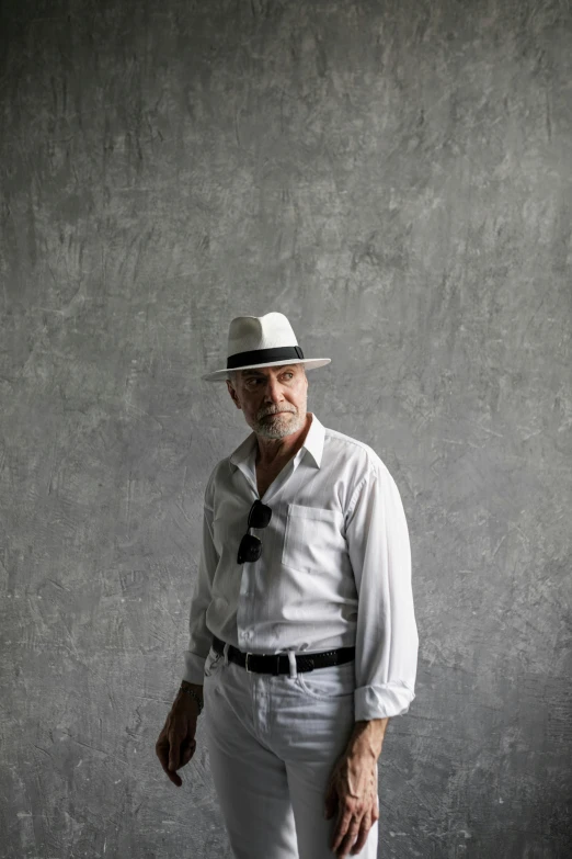 a man in a hat standing in front of a wall, white and silver, grey backdrop, short white beard, in sao paulo