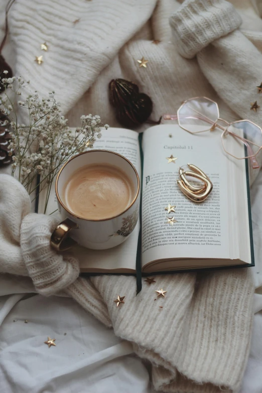 an open book sitting on top of a bed next to a cup of coffee, by Lucia Peka, pexels contest winner, romanticism, gold accessories, winter vibes, relaxed pose, starlit