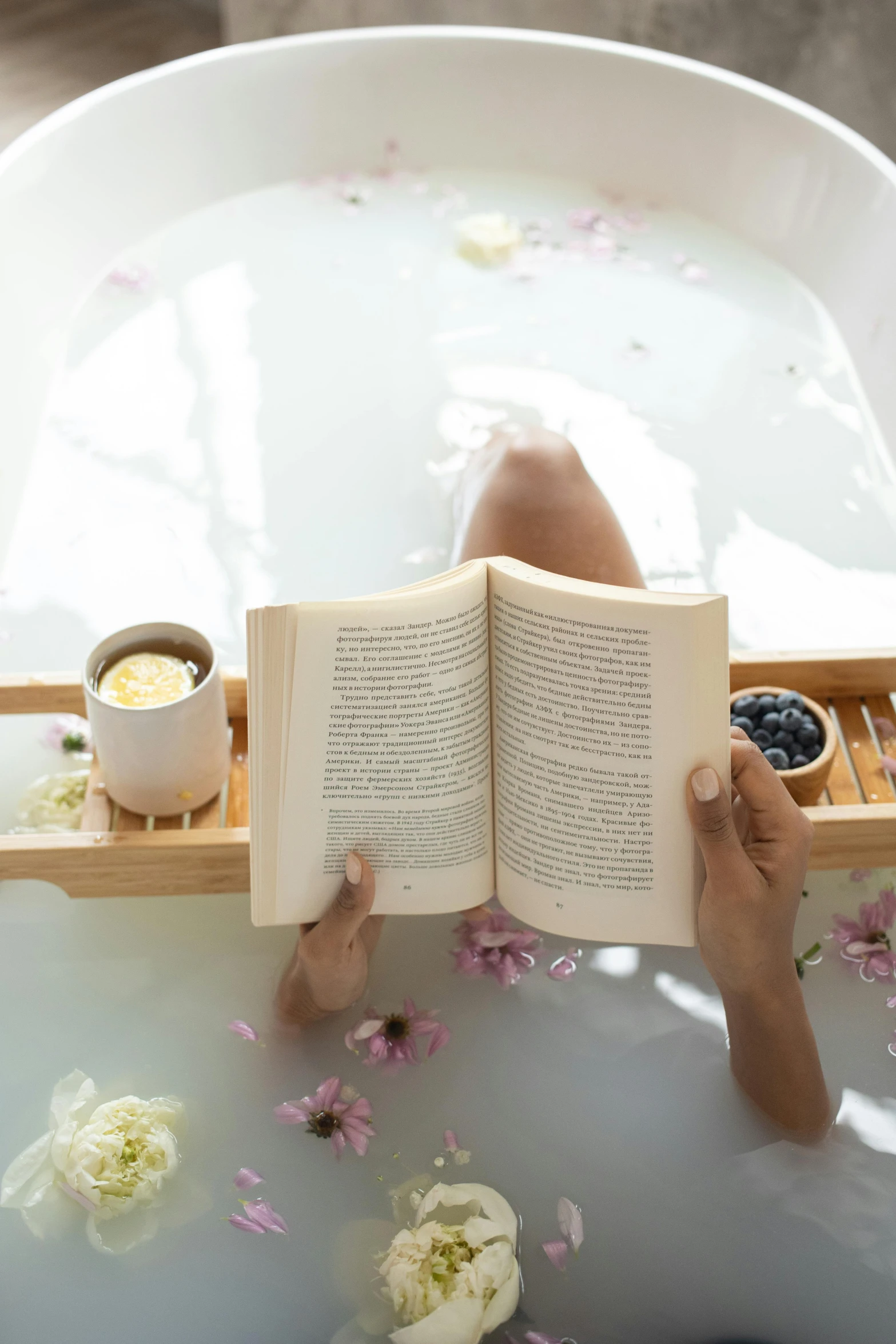 a person laying in a bathtub reading a book, botanicals, handcrafted, vanilla, floating bubbles