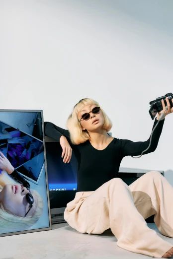 a woman sitting on the ground holding a camera, inspired by Tadashi Nakayama, trending on pexels, video art, portrait of kim petras, sitting on top of a cryopod, television sunglasses, wearing black frame glasses