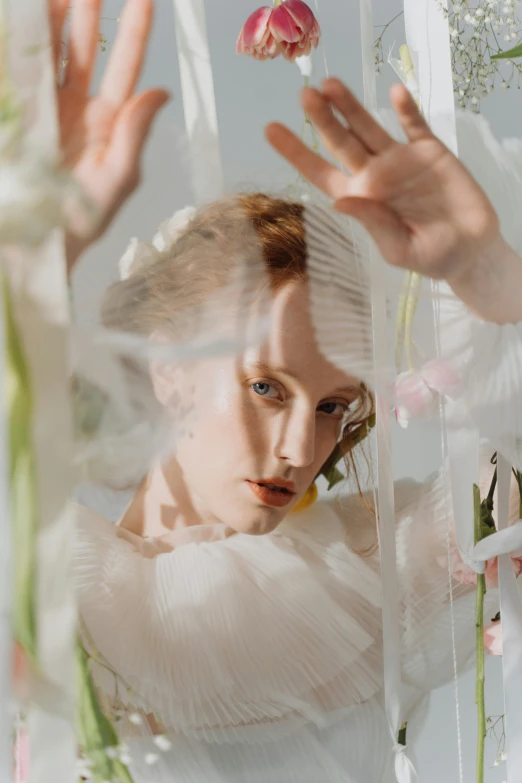 a woman in a white dress surrounded by flowers, inspired by Cecil Beaton, trending on pexels, soft translucent fabric folds, sophia lillis, mirror and glass surfaces, flowing shimmering fabrics