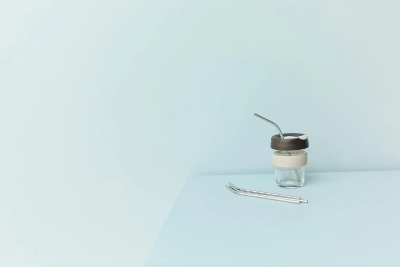 a cup of coffee sitting on top of a table, by Matija Jama, minimalism, glass jar, pastel blue, with a straw, stainless steel