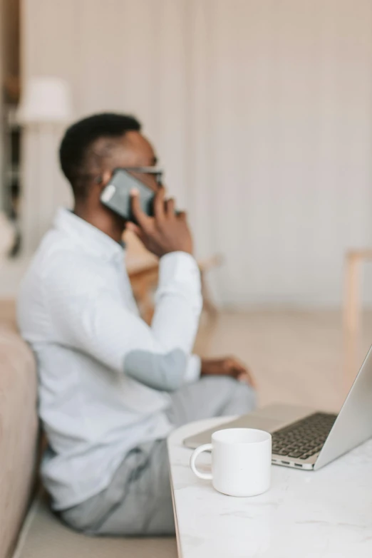 a man sitting on a couch talking on a cell phone, trending on pexels, sitting at a computer, essence, selling insurance, sitting on a mocha-colored table