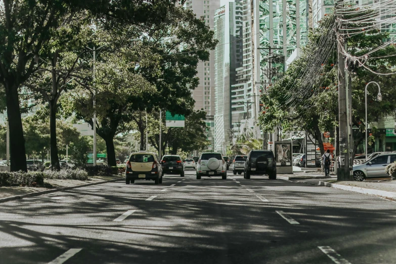 a street filled with lots of traffic next to tall buildings, by Carey Morris, pexels contest winner, philippines, road between tall trees, thumbnail, sunny day time