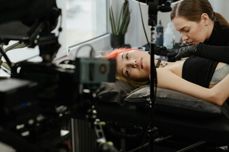 a woman getting a tattoo on another woman's arm, a tattoo, inspired by Elsa Bleda, trending on pexels, hyperrealism, on an operating table, tv commercial, she is laying on her back, cinematic movie photo