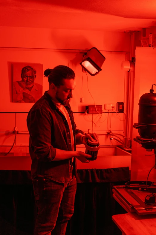 a man standing in a room with a red light, chemical woekshop, art student, concentrated, photograph