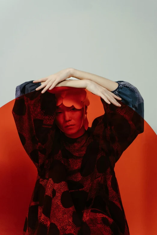 a woman standing in front of a red circle, an album cover, inspired by Taro Yamamoto, trending on pexels, synthetism, orange hue, hands retouched, portrait tilda swinton, asian woman