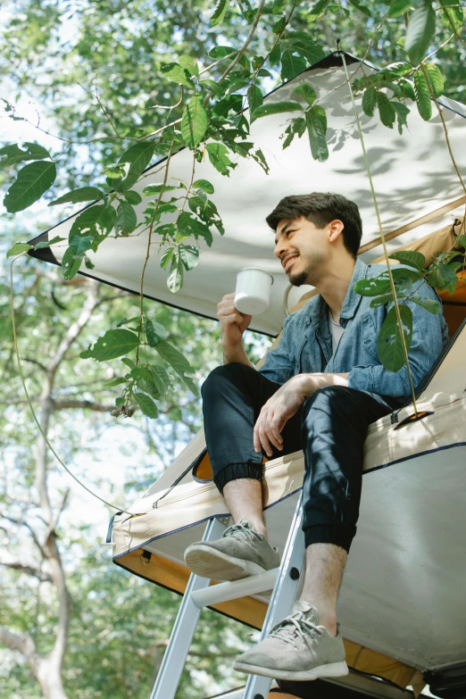 a man sitting on top of a ladder next to a tree, glamping, drinking coffee, wonbin lee, foliage clothing