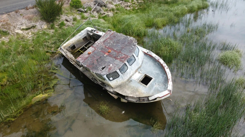 a boat that is sitting in some water, rotting black clay skin, birdseye view, rural wastelands, rhys lee
