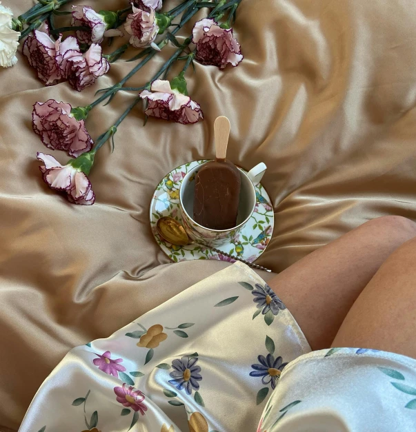 a woman laying on top of a bed next to a cup of coffee, inspired by Konstantin Somov, trending on pexels, rococo, soft silk dress, brown flowers, - 6, silk