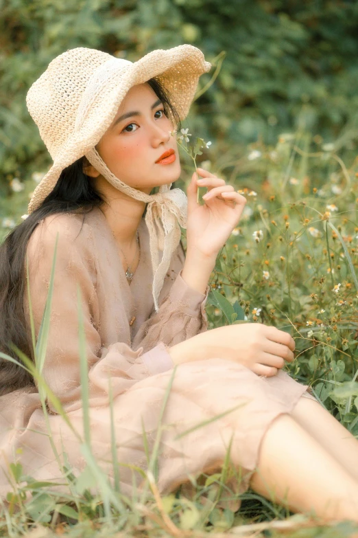 a woman sitting in the grass with a hat on, by Ai Xuan, pexels contest winner, realism, pale thin lips, 中 元 节, warm and soft and subdued colors, handsome girl