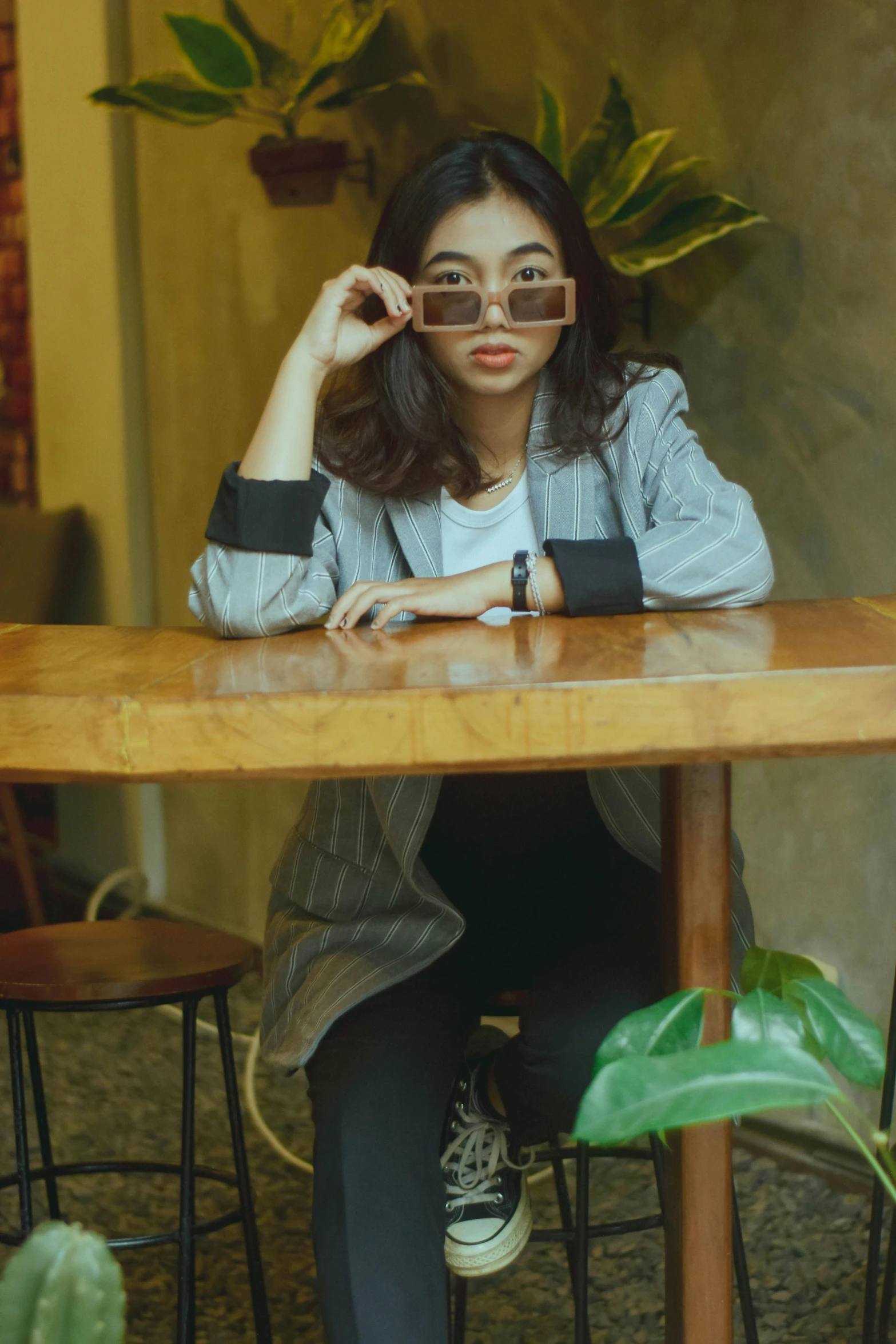 a woman sitting at a table with a camera in her hand, by Basuki Abdullah, looking heckin cool and stylish, sitting on a mocha-colored table, with sunglass, trending photo