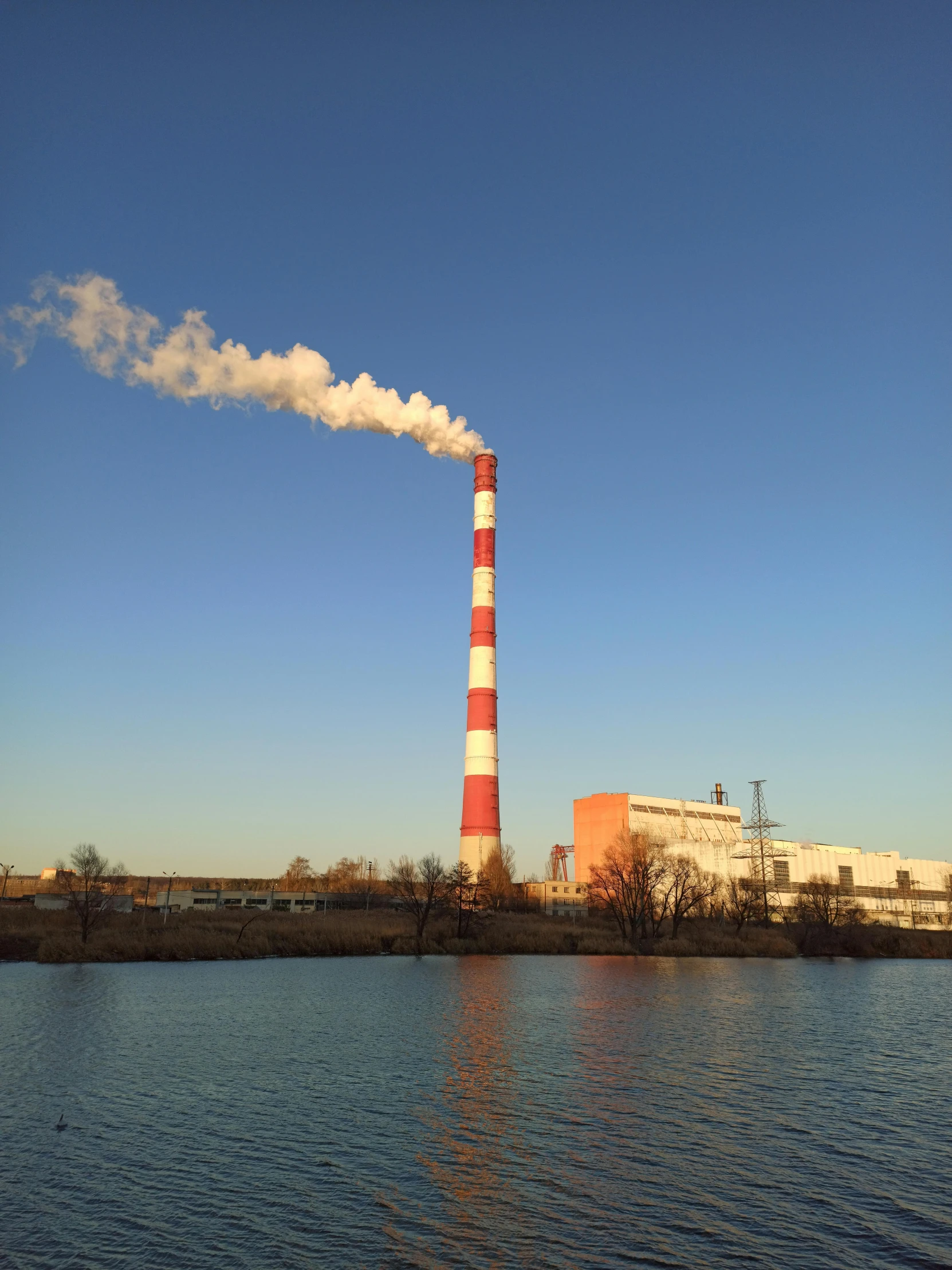 a large body of water with a factory in the background, pexels contest winner, chimney with smoke, tarmo juhola, [32k hd]^10, full frame image