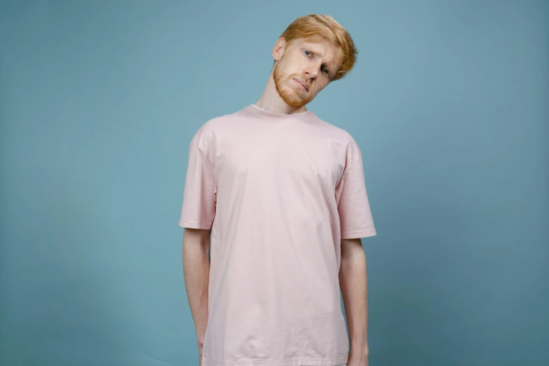 a man with a beard standing in front of a blue background, an album cover, pexels, hyperrealism, pink clothes, extremely pale, wearing a t-shirt, on a pale background
