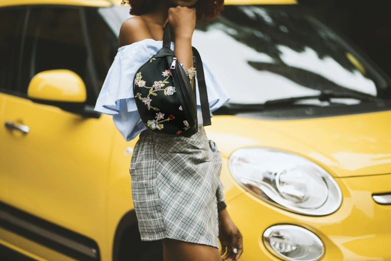 a woman standing in front of a yellow car, trending on pexels, mini skirt, wearing floral chiton, holding a leather purse, trending on imagestation