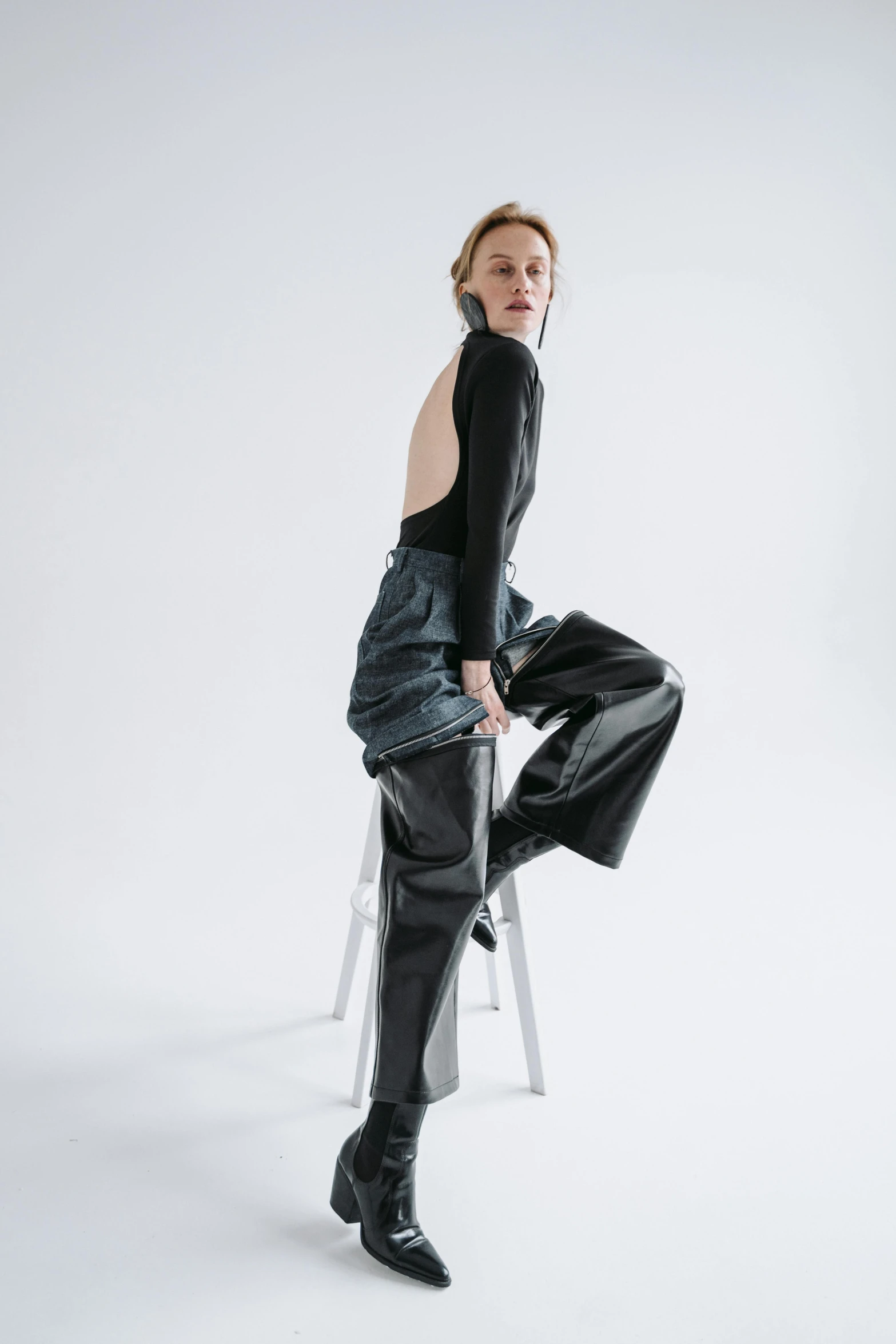 a woman sitting on top of a white chair, by Nina Hamnett, trending on unsplash, dressed in black leather, baggy pants, fashion model features, arched back