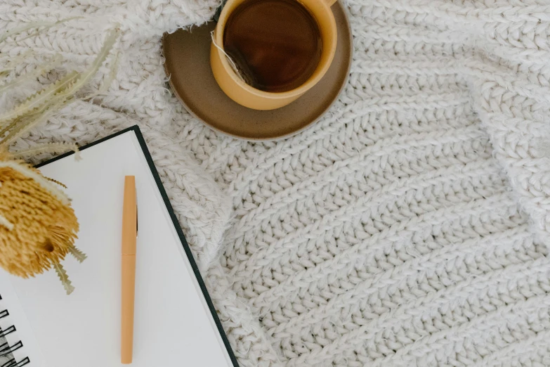 a cup of coffee and a notebook on a bed, trending on pexels, made of wool, background image, jenna barton, white