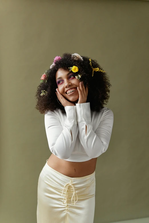 a woman in a white top and skirt posing for a picture, an album cover, trending on pexels, afro made of flowers, wide grin, greeting hand on head, studio shot