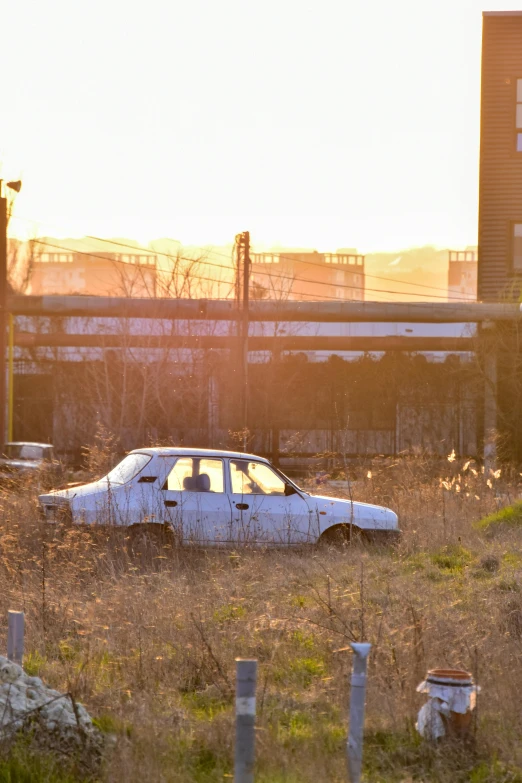 a car that is sitting in the grass, inspired by Elsa Bleda, unsplash, graffiti, abandoned steelworks, late afternoon sun, wide film still, suburb