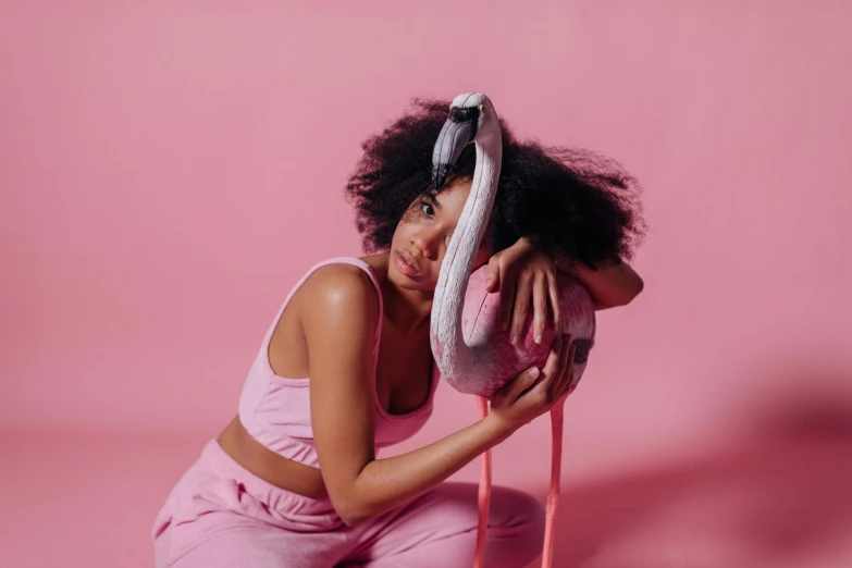 a woman sitting on a pink chair holding a flamingo, trending on pexels, curly afro, wearing a track suit, monochromatic, contorted
