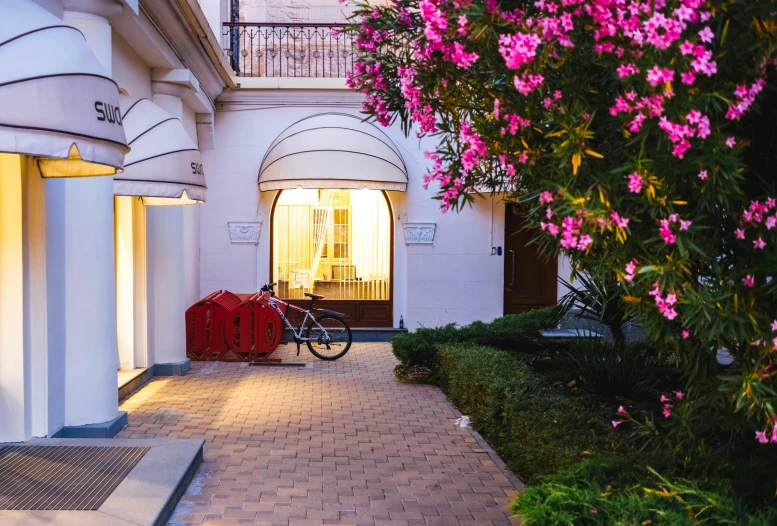 a bicycle is parked in front of a building, by Riad Beyrouti, brightly lit pink room, rose garden, profile image
