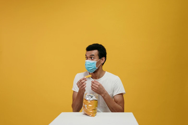 a man wearing a face mask sitting at a table, pexels contest winner, yellow, product shoot, chewing, 1 5 0 4