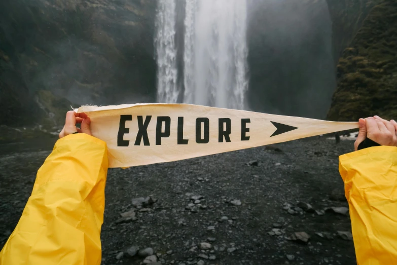 a person holding a sign in front of a waterfall, inspired by national geographic, pexels contest winner, explorer, holding a white flag, exploration, acronym