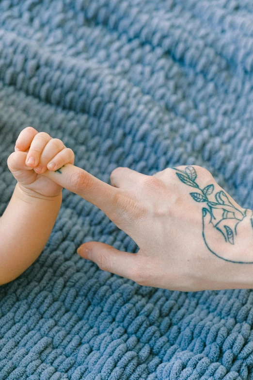 a woman holding a baby's hand on a blue blanket, a tattoo, trending on pexels, pointing index finger, illustration », instagram post, carefully crafted