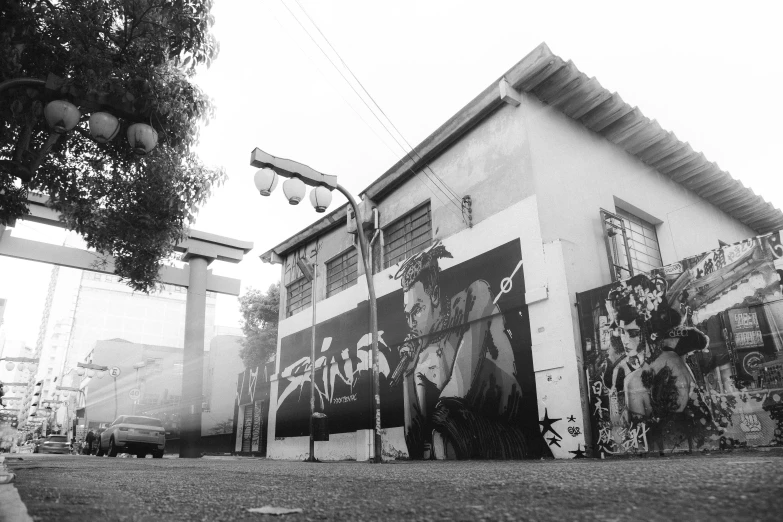 a black and white photo of a mural on the side of a building, by Alejandro Obregón, unsplash, street art, streetlamps, background image, japanese town, gta art