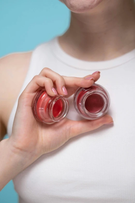 a woman holding two lip bales in her hands, by Nina Hamnett, trending on pexels, red liquid, detailed product image, jelly glow, blush