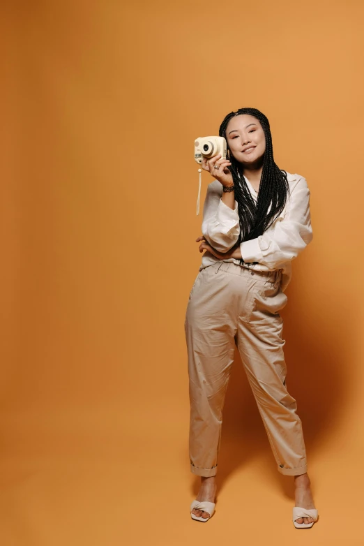 a woman taking a picture with a camera, an album cover, inspired by helen huang, wearing an orange jumpsuit, in a photo studio, wearing white suit, smiling for the camera