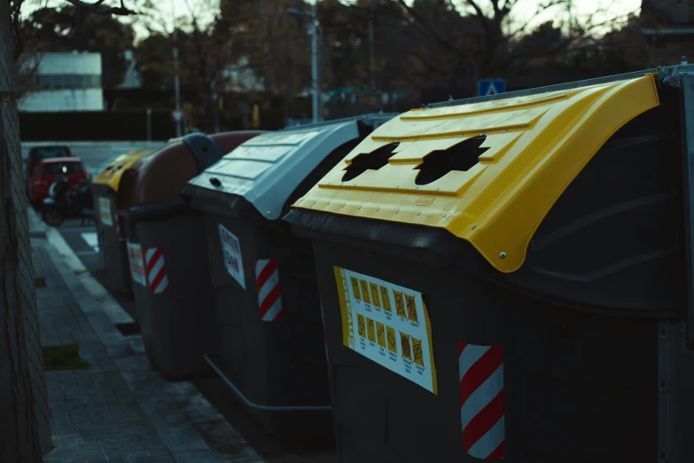 a row of trash cans sitting on the side of a road, a photo, unsplash, plasticien, yellow and black, avatar image