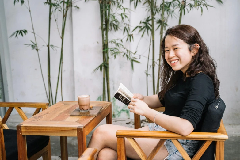 a woman sitting at a table reading a book, inspired by Ruth Jên, pexels contest winner, happening, relaxing and smiling at camera, avatar image, tourist photo, malaysian