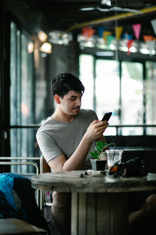 a man sitting at a table looking at his cell phone, pexels contest winner, casually dressed, square, aged 2 5, gif