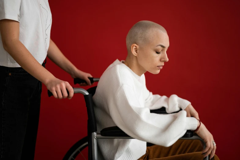 a woman sitting in a wheel chair next to a man, trending on pexels, hurufiyya, a bald, red colored, nursing, derealisation