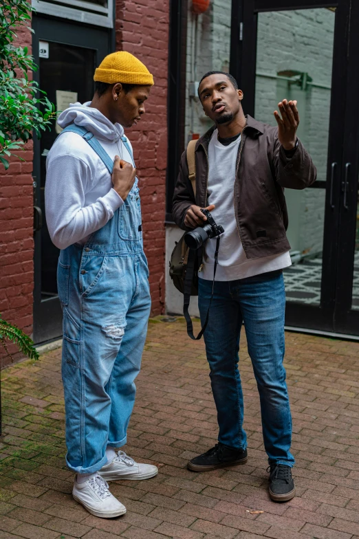 two men standing next to each other in front of a building, a photo, pexels, visual art, wearing blue jean overalls, riyahd cassiem, ( ( theatrical ) ), full body profile camera shot