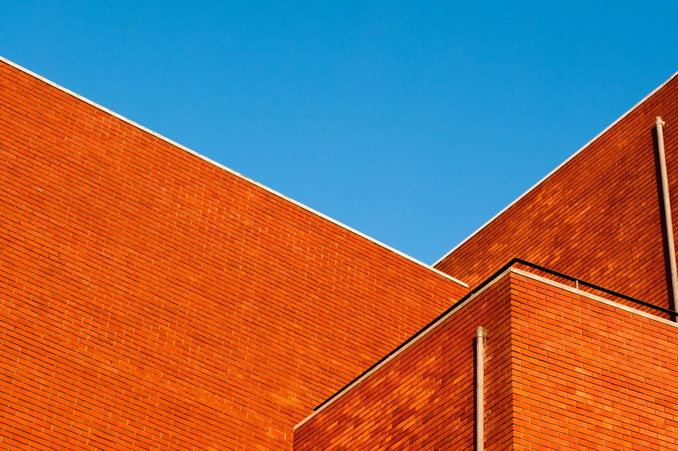 a clock mounted to the side of a brick building, inspired by Bauhaus, unsplash, hypermodernism, clear blue sky, square lines, vibrant orange, clemens ascher