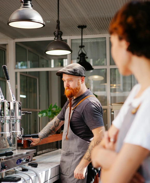 a man and a woman standing in front of a coffee machine, by Lee Loughridge, pexels contest winner, bearded, wearing an apron, thumbnail, beer