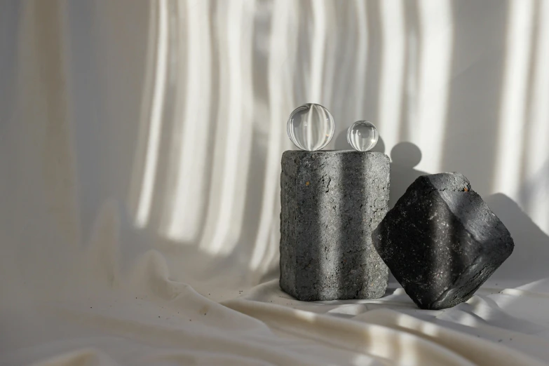 a couple of candles sitting on top of a white sheet, an abstract sculpture, inspired by Kim Tschang Yeul, unsplash, crystal cubism, flying black marble balls, textured base ; product photos, atmospheric crystal dust, glass jar